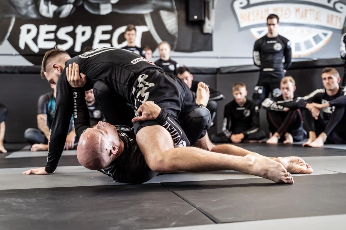A coach demonstrates a technique on the mat while the class watches